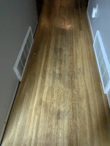 Worn, water-stained hardwood hallway floor before refinishing