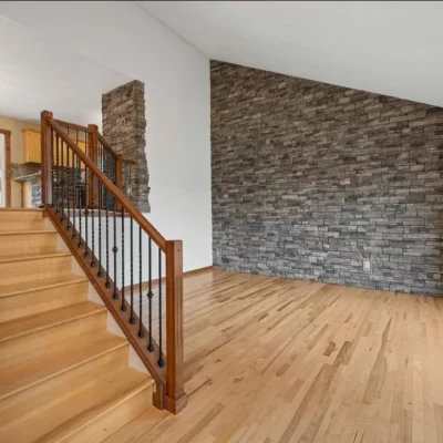 Light hardwood floor and staircase against a stacked-stone feature wall